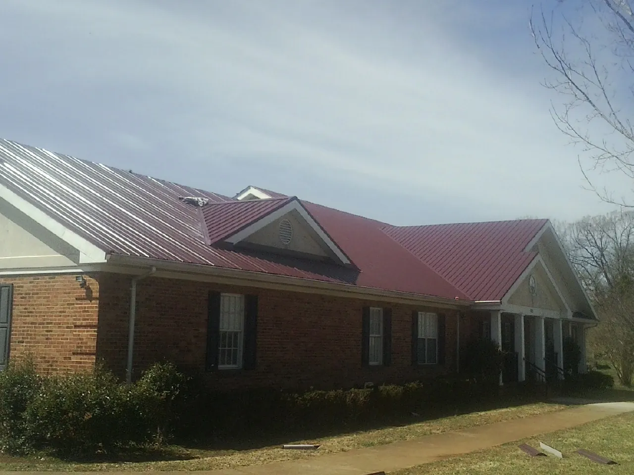 Red metal roof with gabled entries on a long brick building, from a Hail Damage Roof Repair job in Combined Locks
