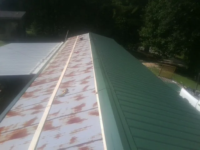Old rusted panels beside newly installed green metal roofing — Wind Damage Roof Repair by Roofing Brothers in Combined Locks