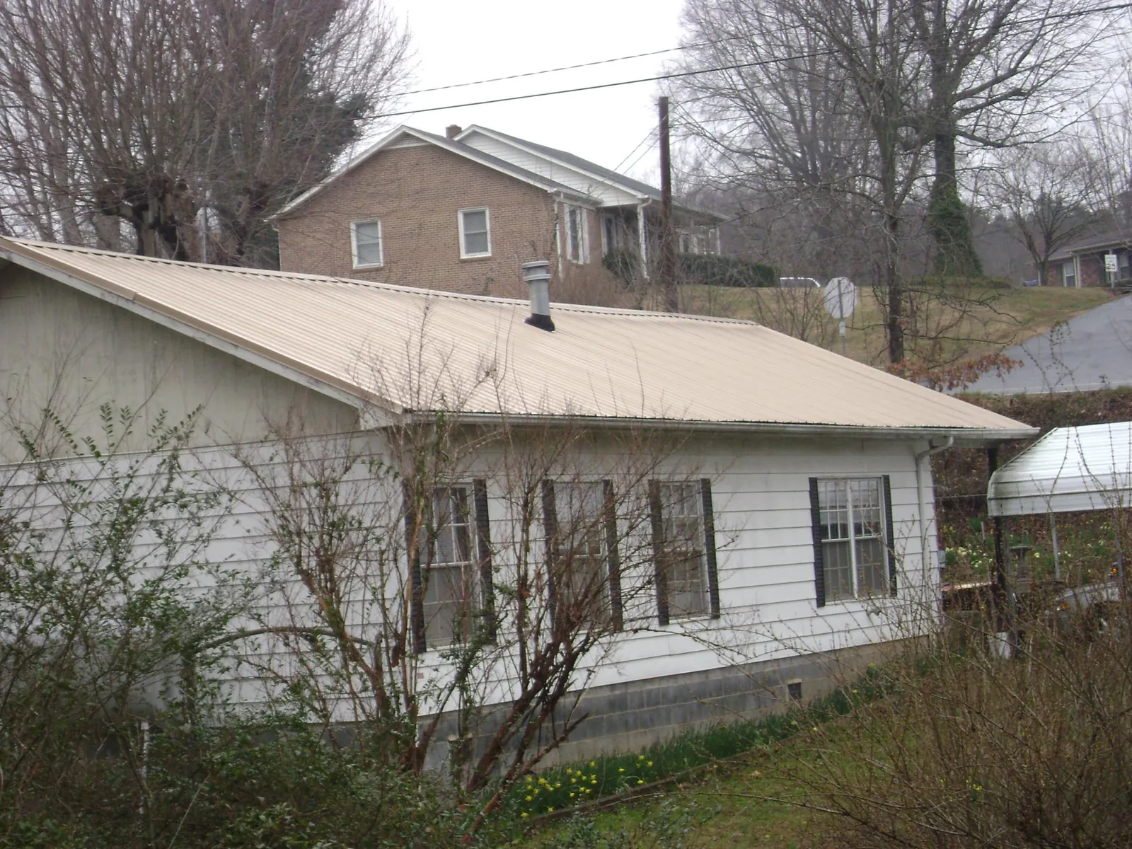 Tan metal roof on a white sided house set into a hillside — Commercial Roofing by Roofing Brothers in Combined Locks