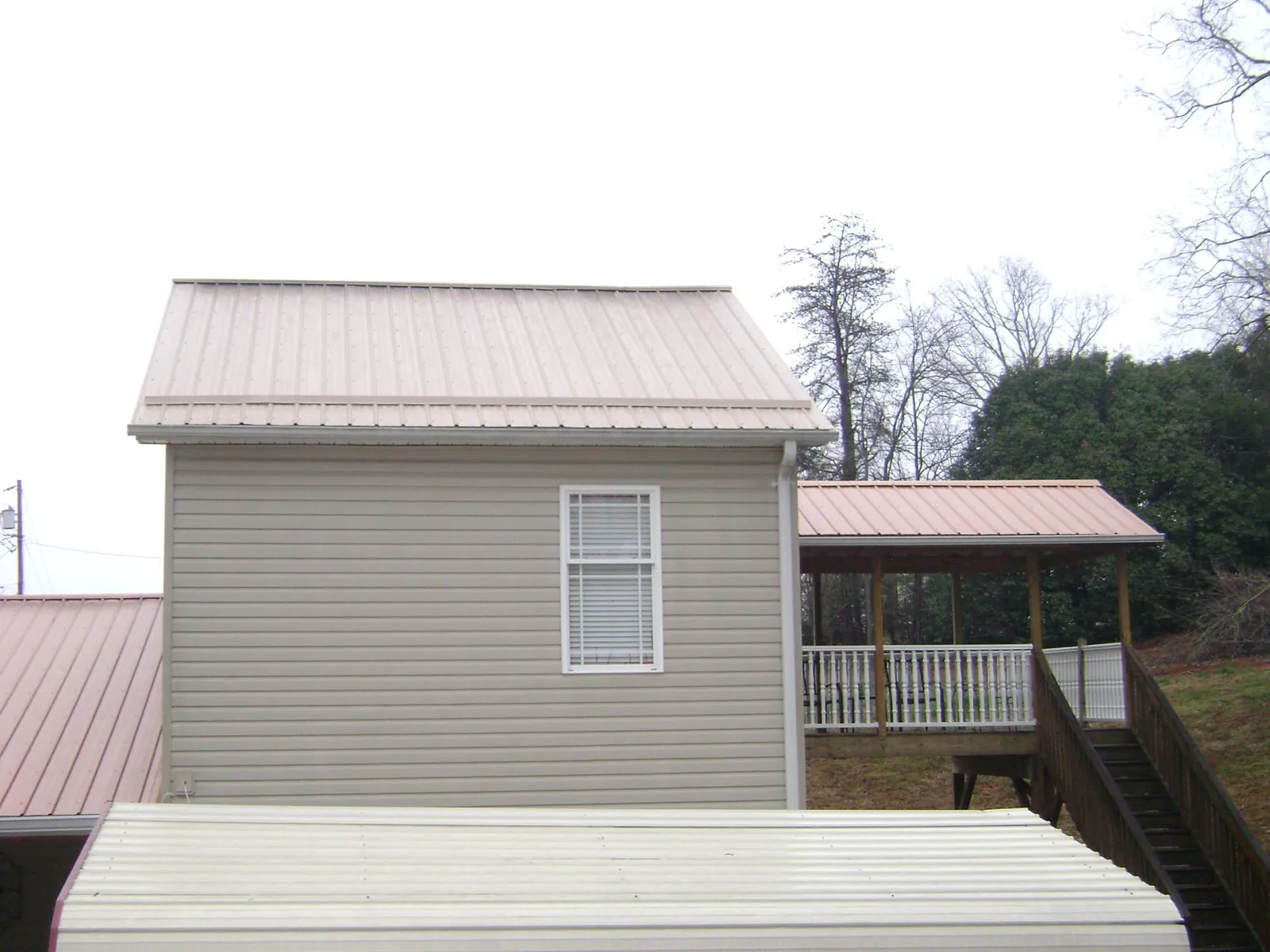Tan metal roofs on a two story addition and attached porch, from a Roof Replacement job in Combined Locks